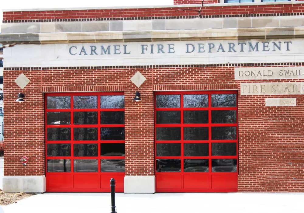Red full-view aluminum sectional doors with tinted glass on a brick fire station