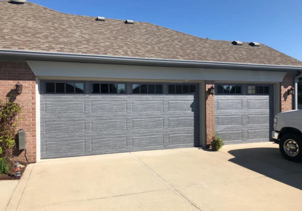 Gray wood-grain long-panel garage doors with window tops on a brick home
